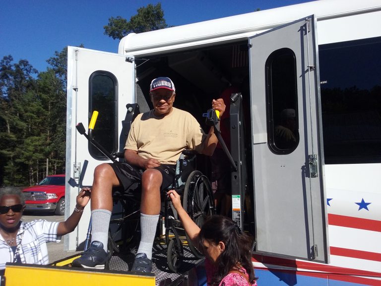 Veteran is lowered using the wheelchair lift on the bus