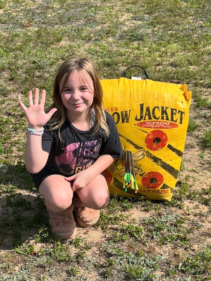 Young archer holds up 5 fingers for 5 arrows in her bullseye on her target