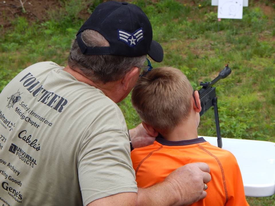 young boy aims an air rife with the guidance of a volunteer instructor