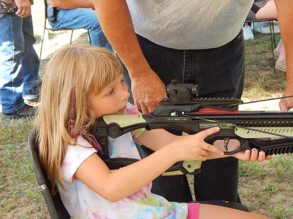 young archer aims her crossbow with the help of an instructor