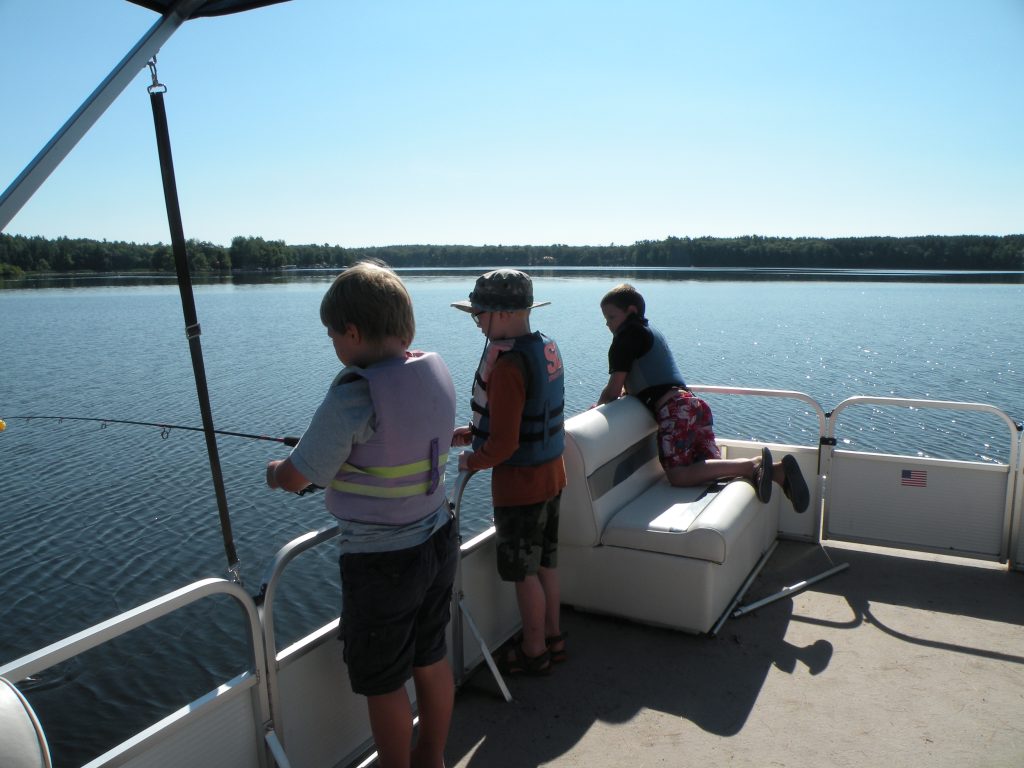 three kids look over the side of the boat on a fishing trip
