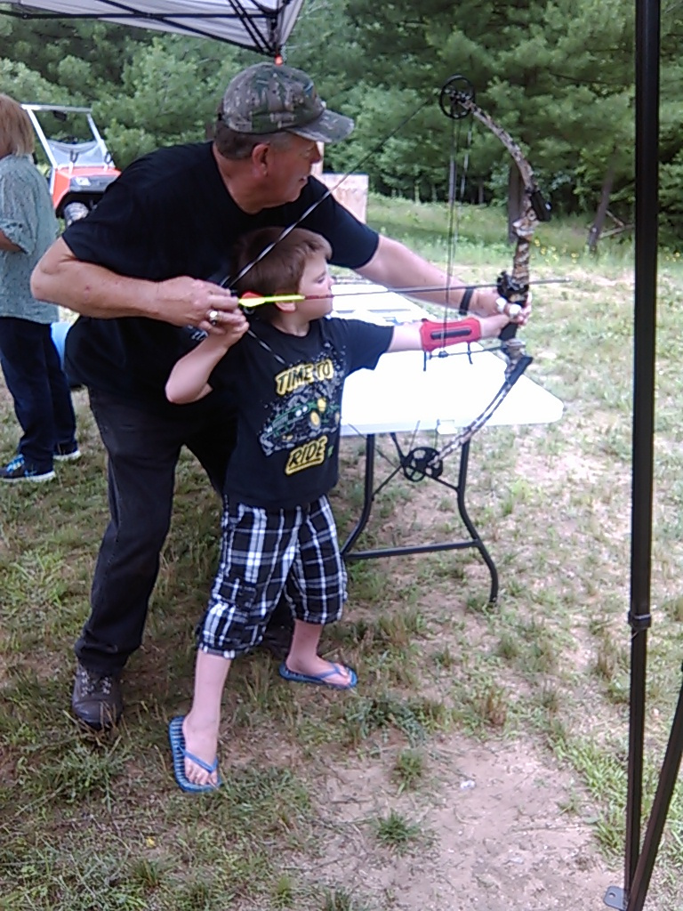 youth archer pulls back and aims his bow with the help of an instructor