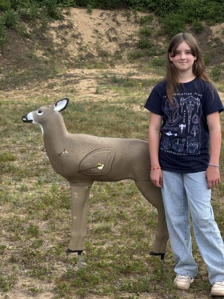 young archer stands next to her deer decoy target