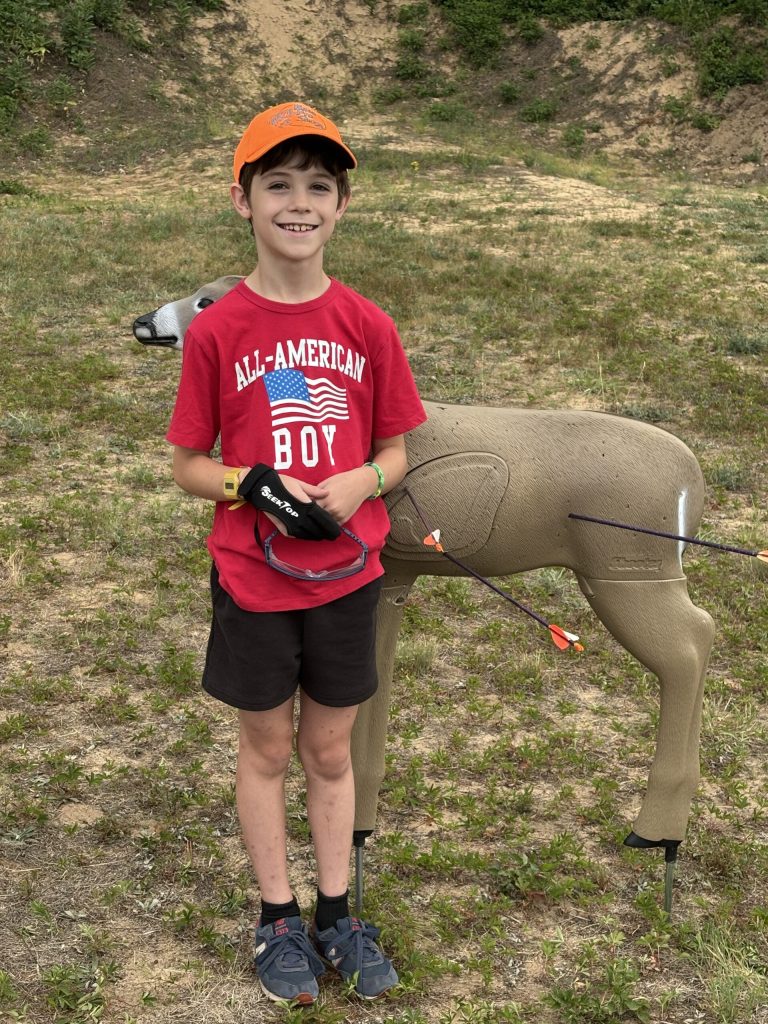 young archer stands next to his deer decoy target